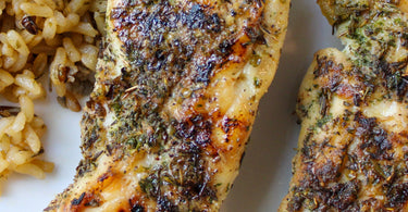 Grilled garlic and herb chicken tenderloins served with brown and wild rice, garnished with fresh herbs and sliced radishes on a white plate.