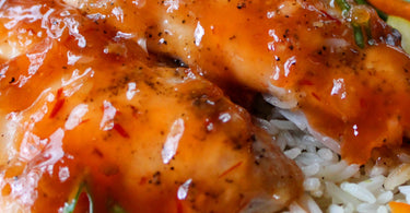 Juicy oven-baked sweet chili chicken tenderloins coated in an orange chili sauce, served over fluffy white rice with fresh herbs and sliced peppers.
